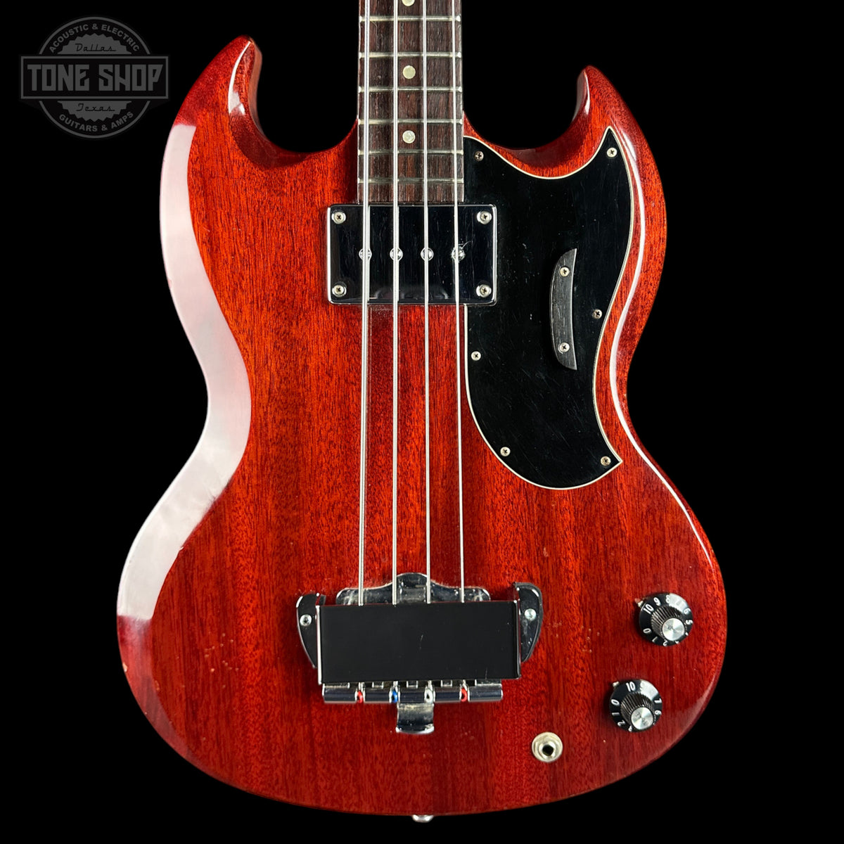 Red electric bass guitar with a black pickguard on a black background, featuring the Tone Shop logo.