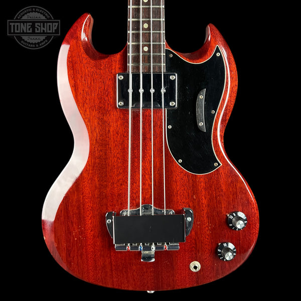 Red electric bass guitar with a black pickguard on a black background, featuring the Tone Shop logo.