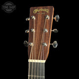 Close-up of the headstock of a Martin & Co acoustic guitar, showing six tuning pegs, six strings, and the gold-foiled brand logo on a dark brown wood background, set against a solid black backdrop.