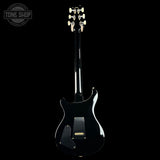 A black electric guitar shown from the back against a solid black background, featuring a glossy finish and gold hardware.