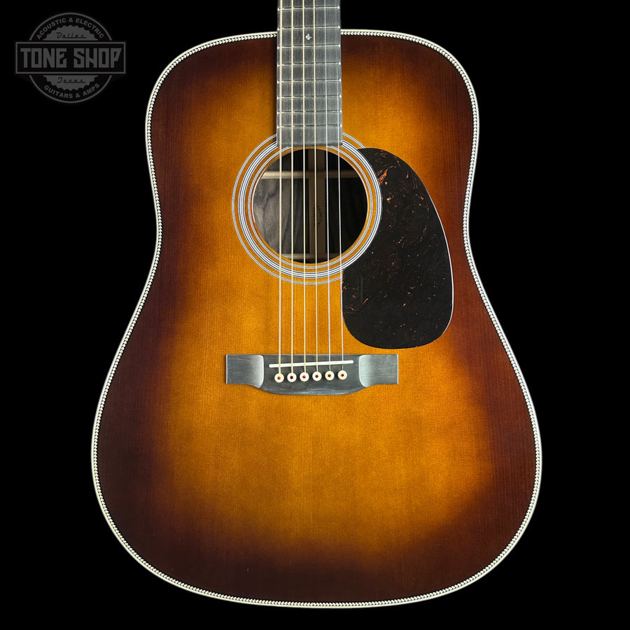 A classic acoustic guitar with a sunburst finish, featuring a dark brown outer edge fading to a warm amber-orange center, set against a solid black background.