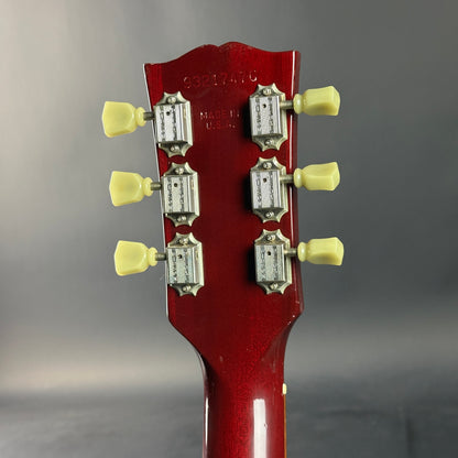 Close-up of a red guitar headstock with tuning pegs on a gray background