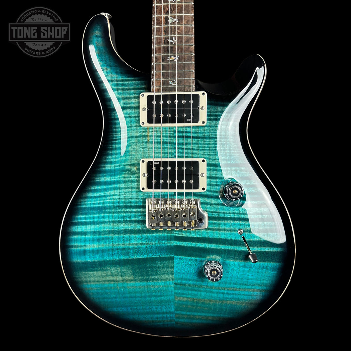 A close-up of a turquoise and teal electric guitar body with a flamed maple wood finish, featuring chrome hardware, a dark fretboard, and a black background. A Tone Shop watermark is visible in the top left corner.