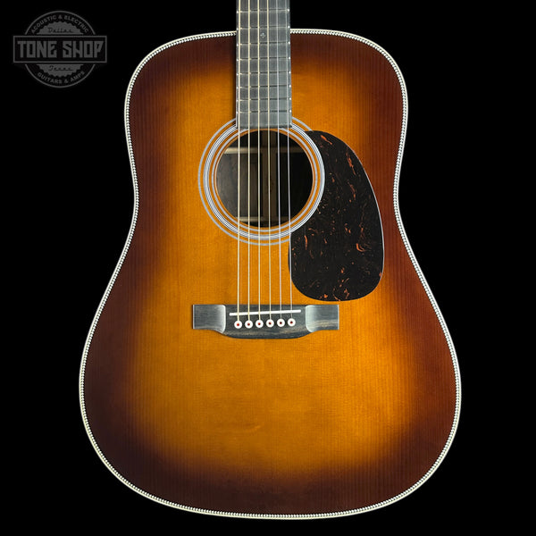 A classic acoustic guitar with a natural sunburst finish, featuring a dark black pickguard and a white binding around the body, shown against a solid black background with a Tone Shop logo in the top left corner.