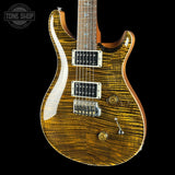 A close-up of an electric guitar body with a glossy flamed maple wood finish showing prominent golden-brown grain patterns, set against a solid black background. A Tone Shop watermark is visible in the top-left corner.