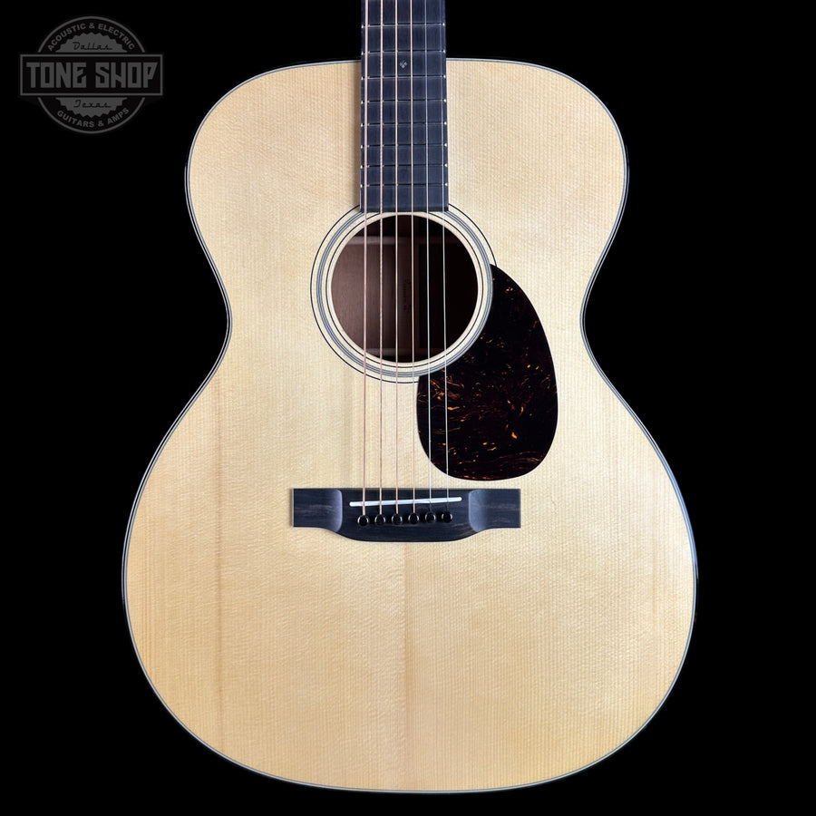 An acoustic guitar with a natural light wood finish and a dark pickguard, shown from the front against a solid black background. A 'TONE SHOP' watermark is visible in the top-left corner.