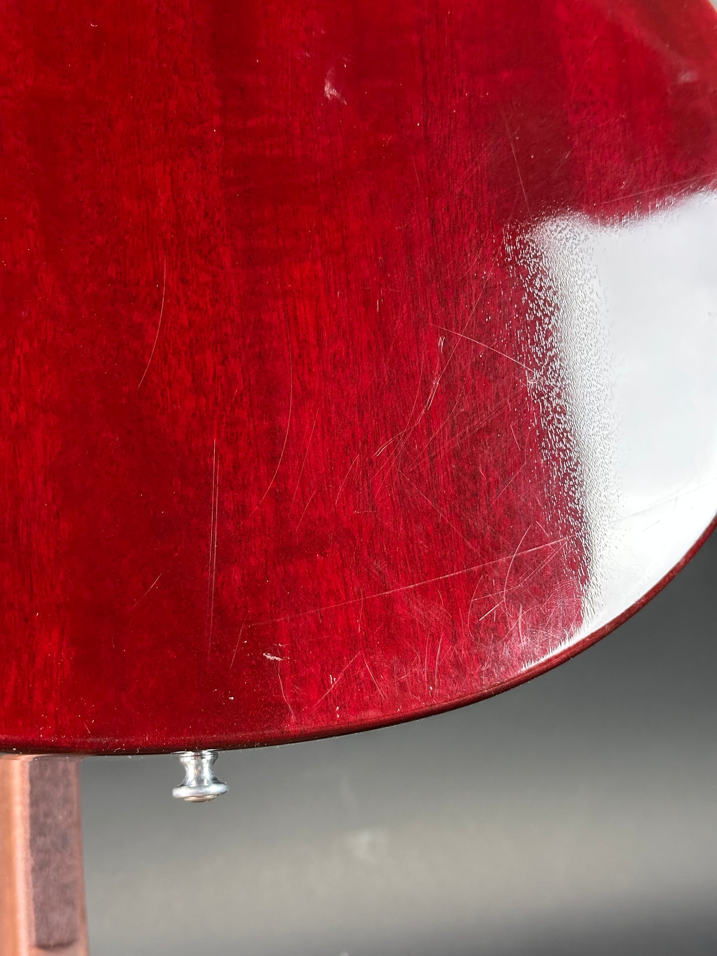 Close-up of a red guitar body with visible scratches and a screw.