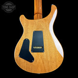 Close-up of the back of an electric guitar body in a natural wood finish, showing a black pickguard and control plate against a black background. A Tone Shop watermark is visible in the top left corner.
