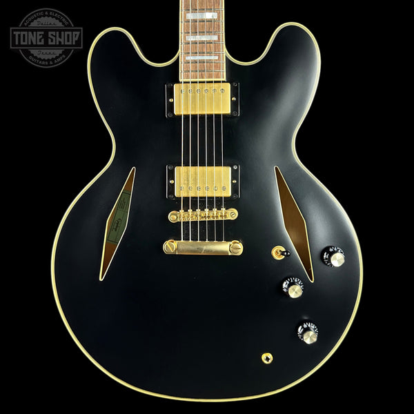 Black electric guitar with gold hardware on a black background, featuring 'Tone Shop' logo.