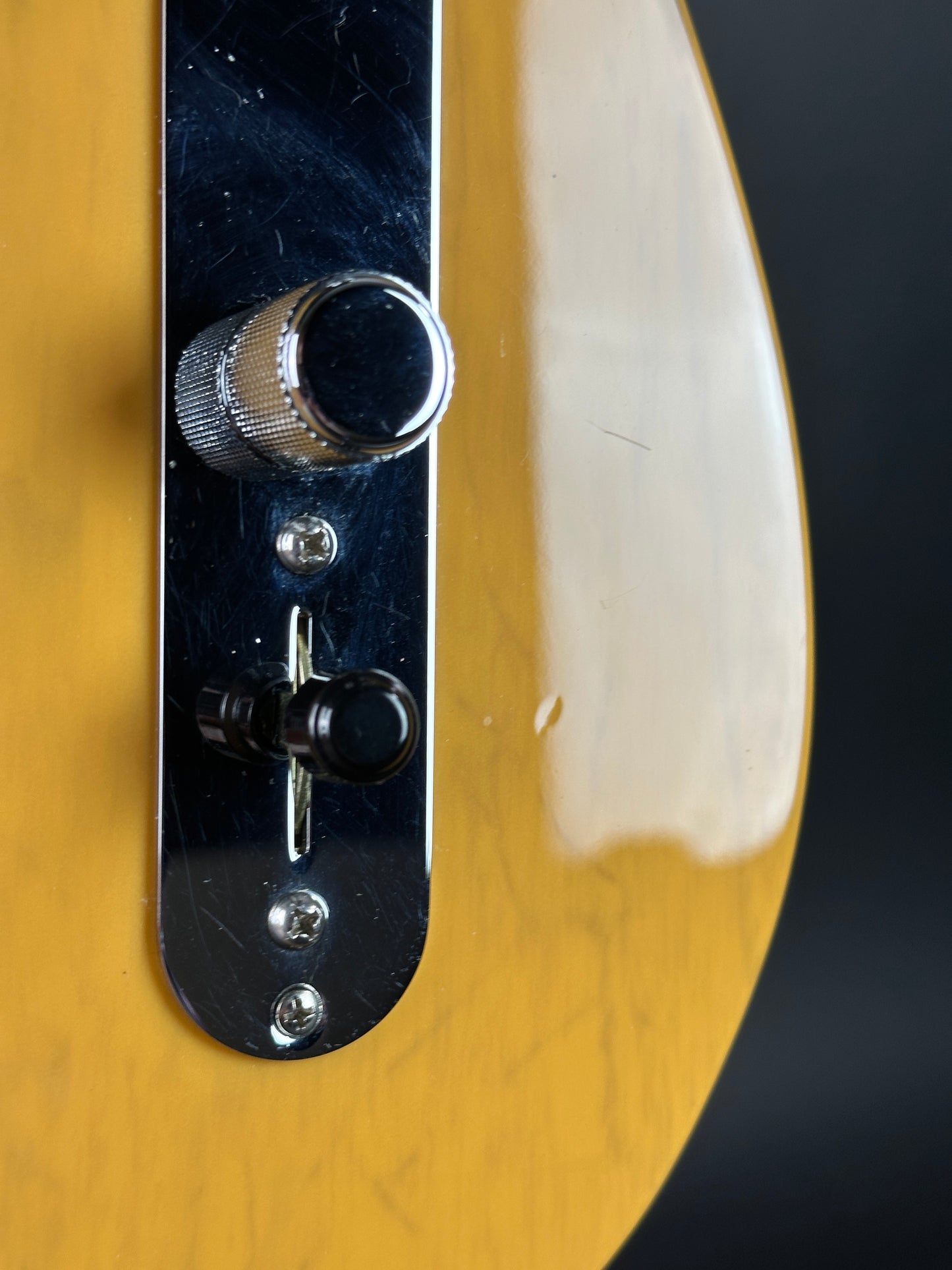Close-up of a guitar control panel with knobs on a wooden guitar body.