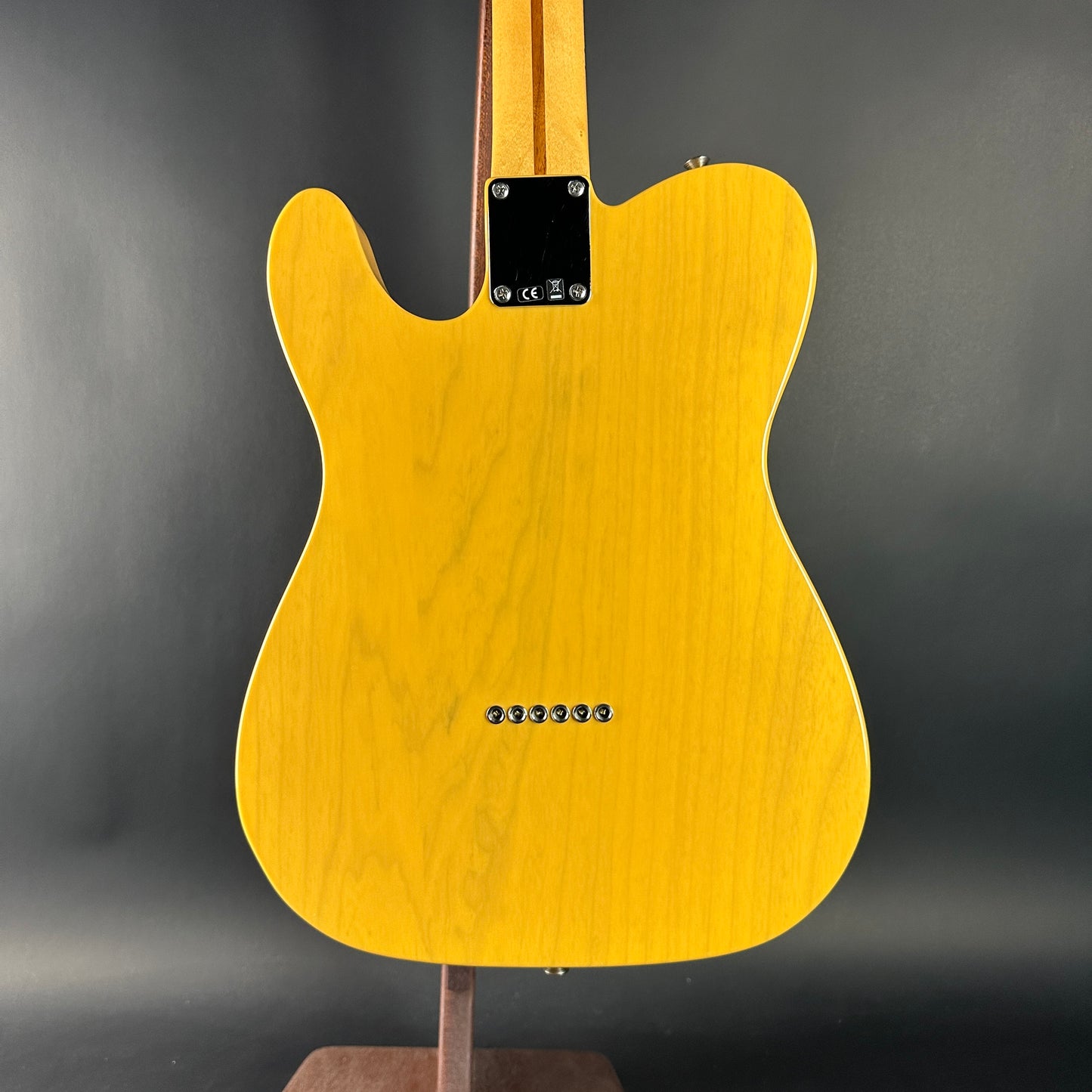Yellow electric guitar on a stand against a gray background
