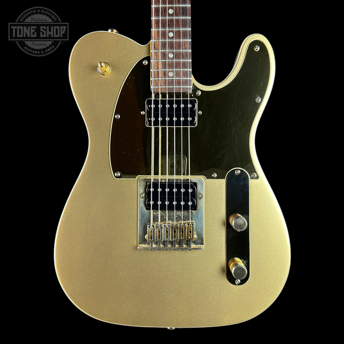 A gold-finish electric guitar with a black pickguard and chrome hardware, shown against a solid black background. A Tone Shop watermark is visible in the top-left corner.