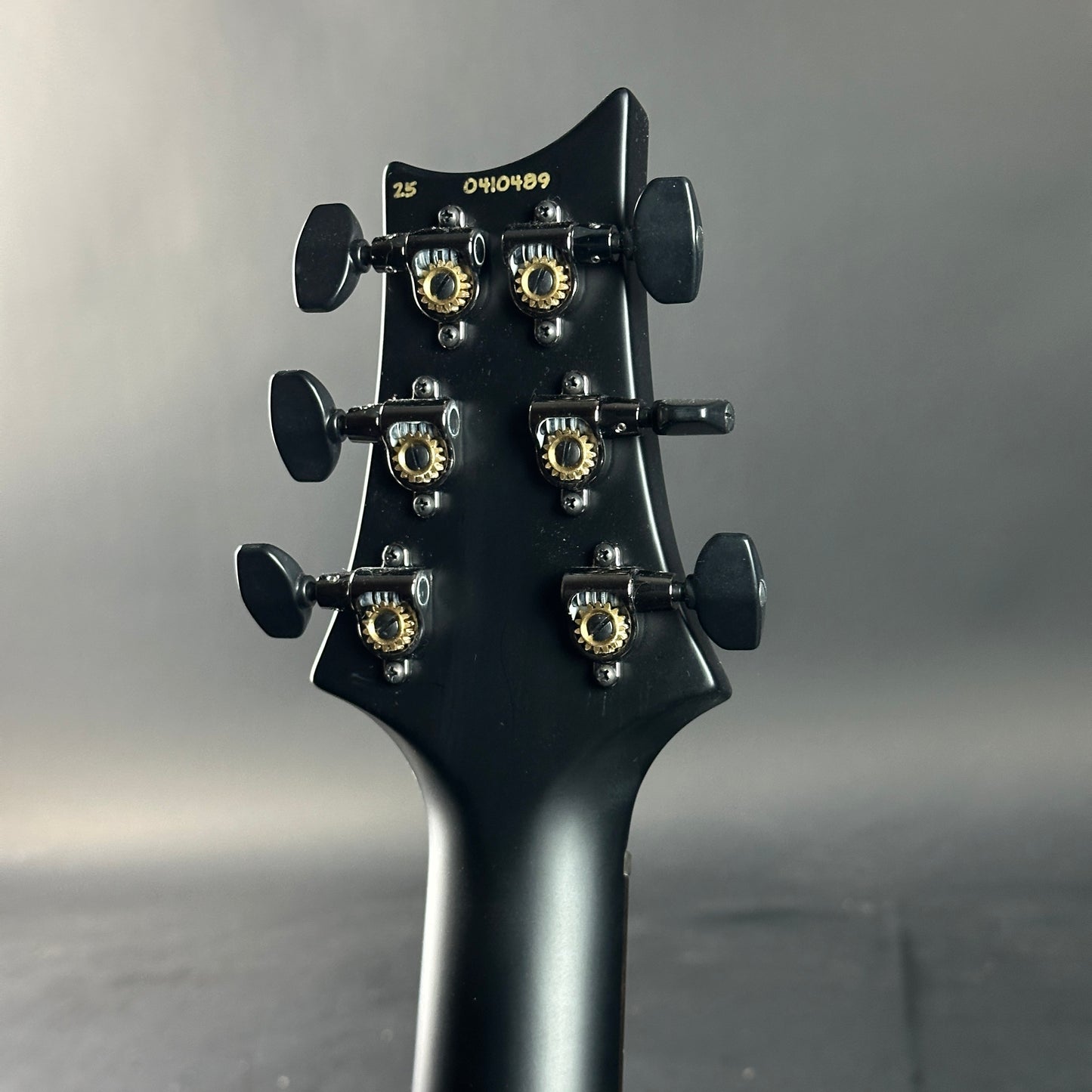 Close-up of a black guitar headstock with tuning pegs on a gray background