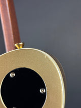 Close-up detail of a gold metallic guitar body with a black circular plate and visible screws, alongside a brown neck against a dark gray background.