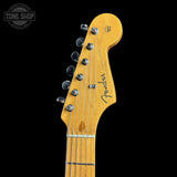 Close-up of a Fender Stratocaster electric guitar headstock in a natural maple finish, featuring six silver tuning pegs and a black script signature, set against a solid black background.