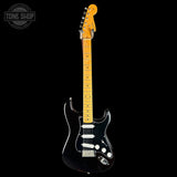 A black electric guitar with a yellow maple neck and headstock, photographed against a solid black background. A Tone Shop watermark is visible in the top-left corner.