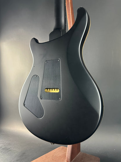 Close-up of a black electric guitar body with a visible brand logo on a gray background