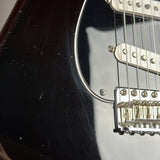 Close-up of a black electric guitar body with white pickups and a chrome bridge, showing visible wear, scratches, and dust on the glossy finish.