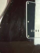 Close-up of a black electric guitar body with a silver pickguard and visible scratches on the glossy finish.