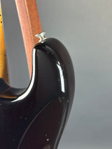 Close-up of the glossy black body of a guitar, showing the side contour and a small silver hardware detail against a gray background.