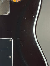 Close-up of the side body of an electric guitar, showing a glossy black finish with a white edge trim, a black pickguard, and a silver metal plate.
