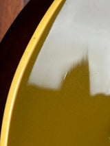 Close-up detail of a glossy olive green surface with a yellow rim and a dark brown base, showing a reflection on the top layer.
