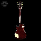 A dark reddish-brown electric guitar shown from the back against a solid black background, featuring a glossy finish, cream-colored pickguard, and gold tuning pegs.