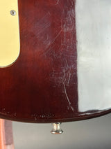 Close-up of a glossy dark brown wooden guitar body with visible scratches on the finish, a cream pickguard, and a silver control knob against a neutral gray background.