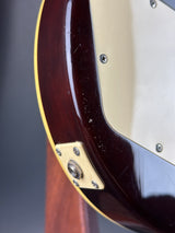 Close-up detail of an electric guitar body showing a glossy dark brown wood finish, cream pickguard, gold hardware, and a thin gold edge stripe.