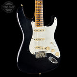 Black electric guitar with a white pickguard on a black background, featuring the Tone Shop logo.