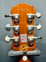 Guitar headstock with tuning pegs and brand logo on a gray background