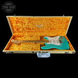 Turquoise electric guitar in an open gold case with a 'Tone Shop' logo.
