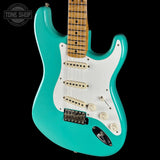 Turquoise electric guitar with a white pickguard on a black background, featuring the Tone Shop logo.