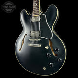 Black electric guitar with a 'Tone Shop' logo in the corner