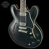 Black electric guitar with a glossy finish on a black background, featuring the Tone Shop logo.