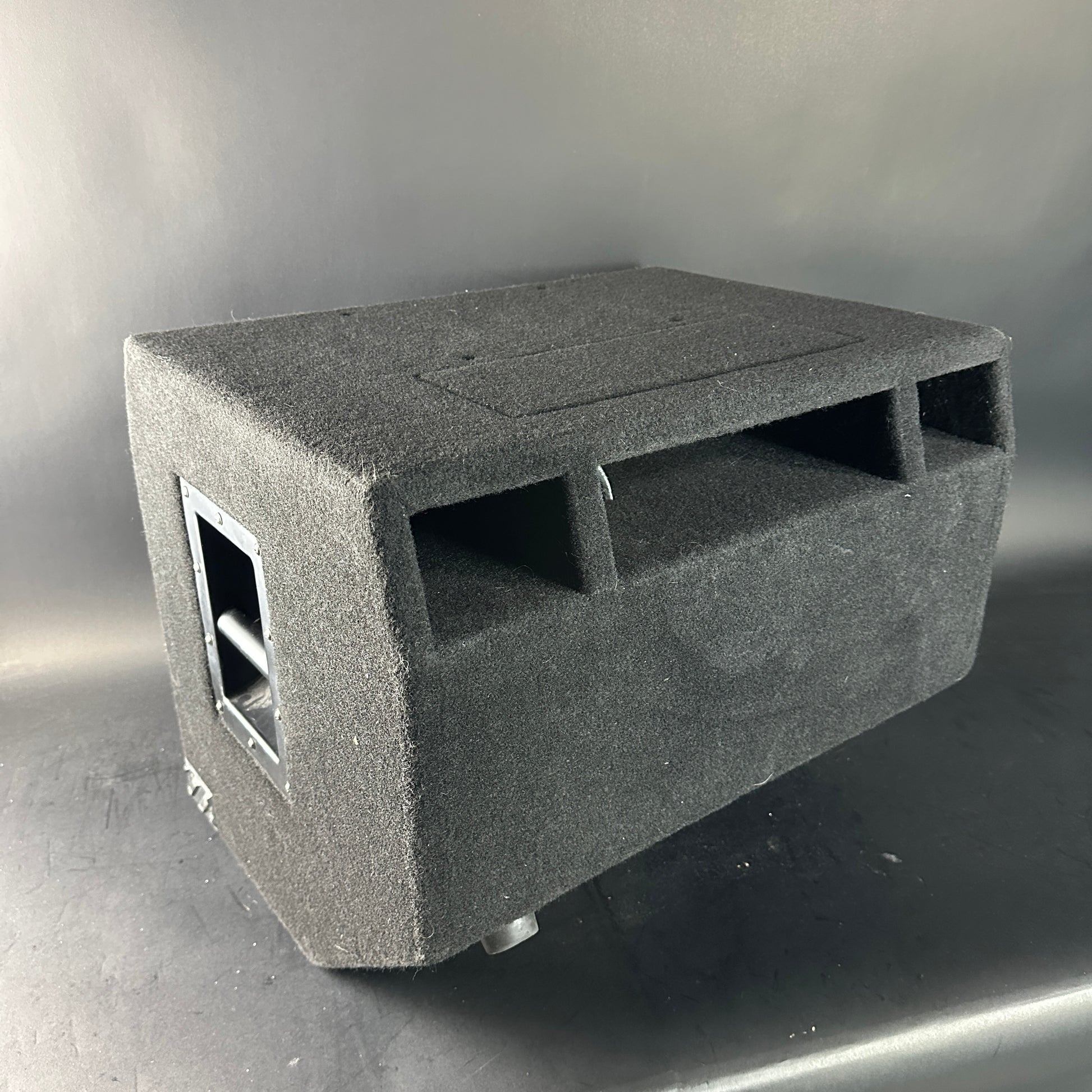 Gray subwoofer enclosure on a reflective surface with a neutral background