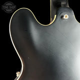 Close-up of a black guitar body with a visible brand logo in the corner.