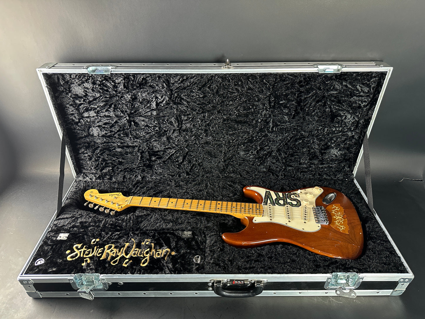 Guitar in a case with 'Stevie Ray Vaughan' branding on a gray background