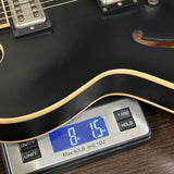 Digital scale measuring a black electric guitar on a wooden surface