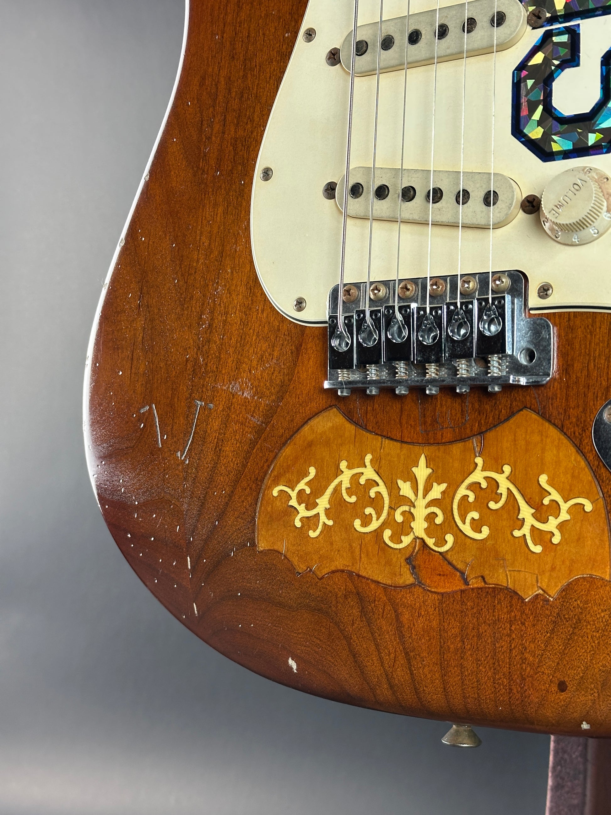 Close-up of a wooden electric guitar with intricate inlay on a gray background