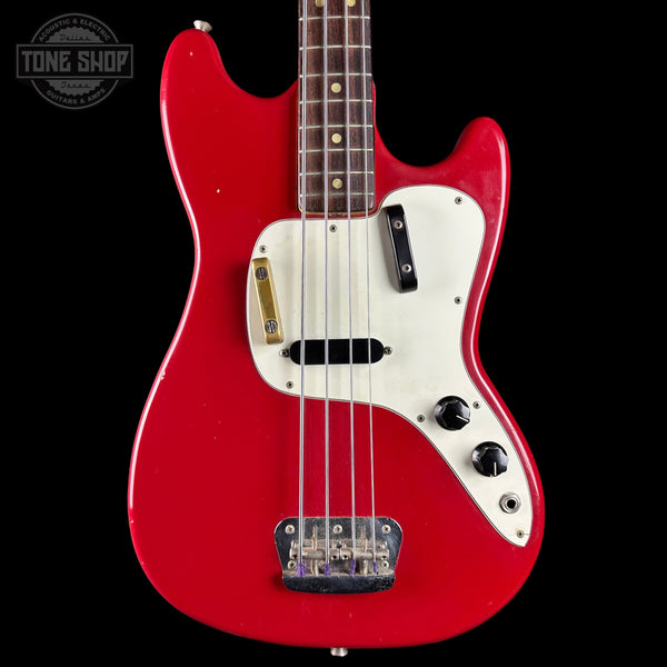 A red electric bass guitar with a white pickguard, black controls, and gold hardware, shown against a black background with a Tone Shop watermark in the top left corner.