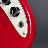 Close-up of a red electric guitar body showing part of a white pickguard, black control knobs, and a metal jack connector against a dark gray background.