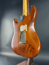Close-up of a wooden guitar body with visible wear and signatures on a gray background