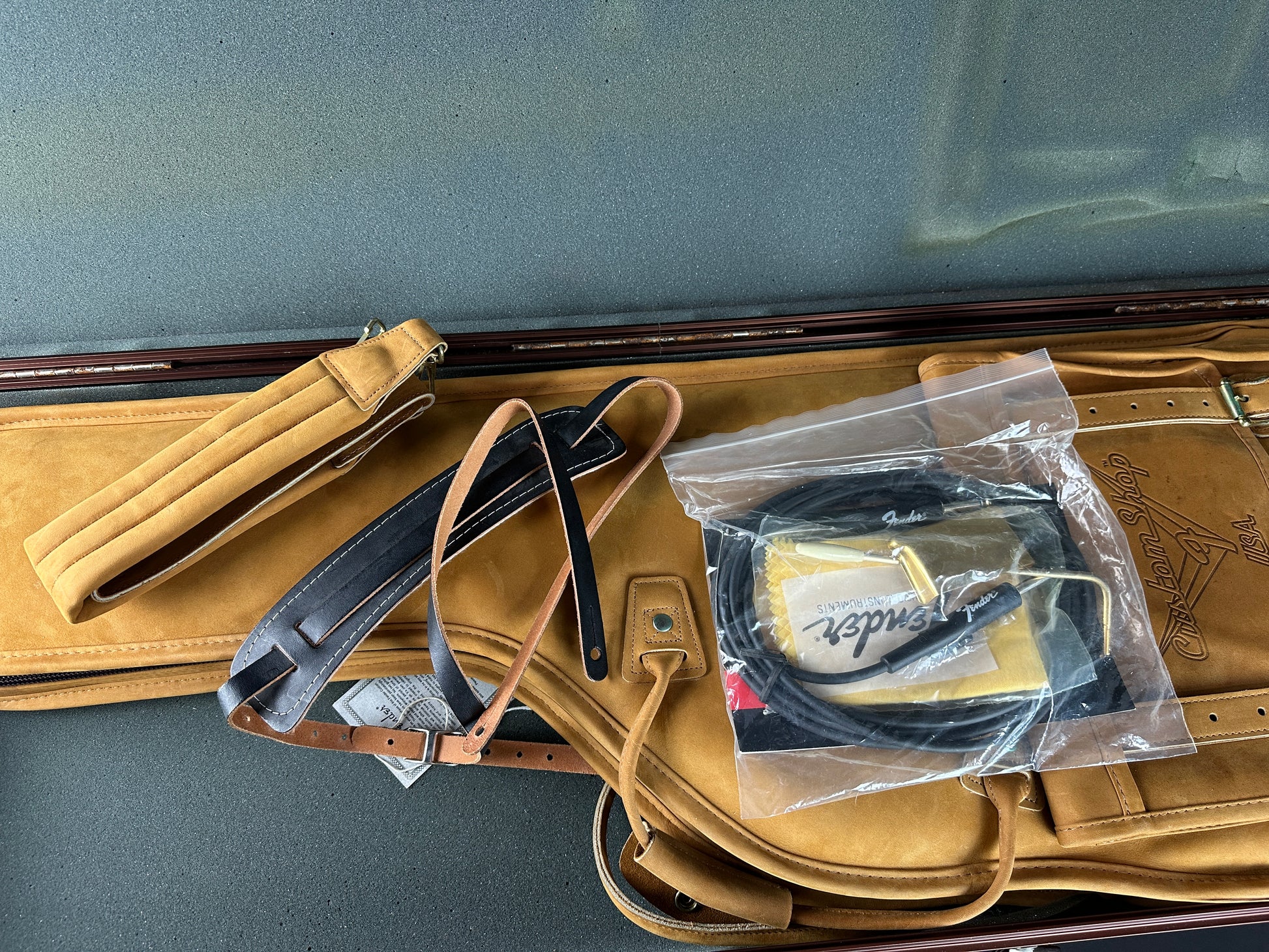 Tan leather case with black straps and a clear plastic bag containing a black item on a gray surface.
