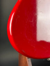 Close-up of a glossy red guitar body showing the glossy finish, minor scuffs, and a hint of a wooden neck on the right side.