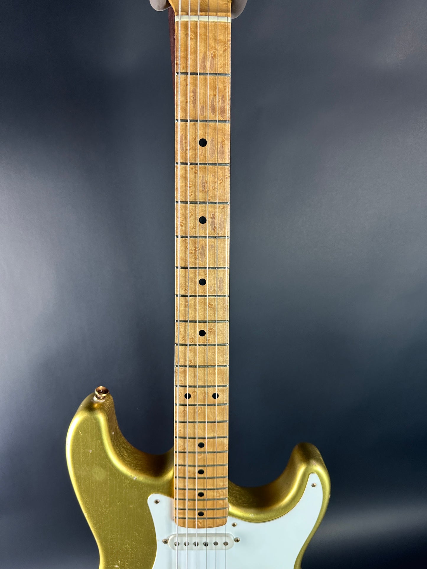 Electric guitar with gold body and white pickguard on a dark background