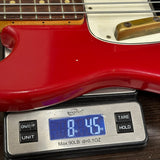 A red electric bass guitar body resting on a digital scale displaying 8 lbs 4.5 oz, with the neck and strings partially visible.