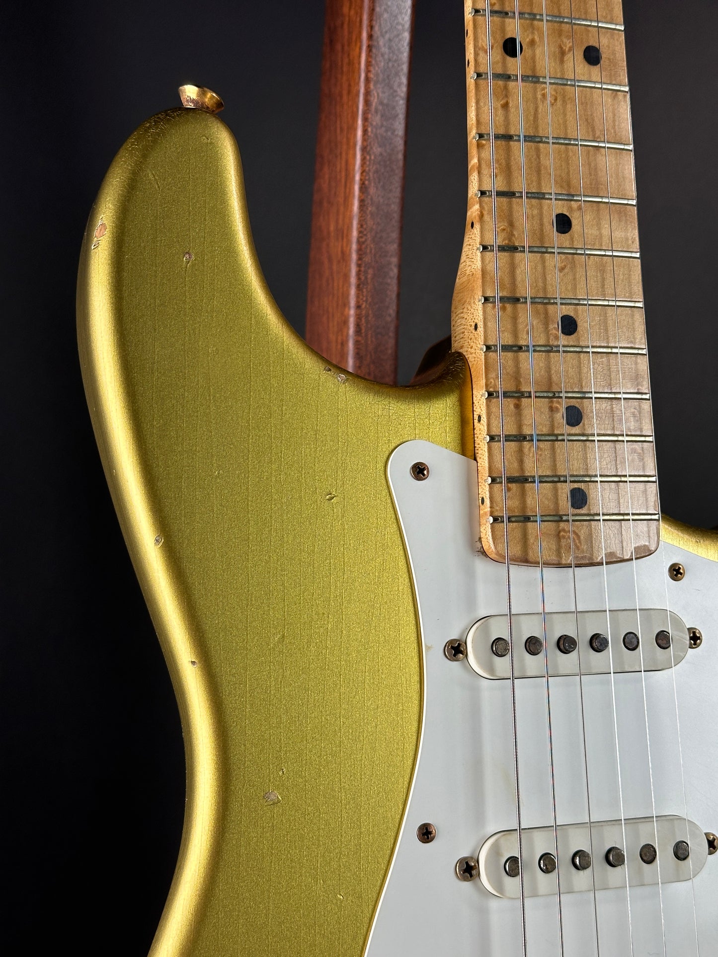 Close-up of a guitar with a gold body and wooden neck on a black background