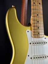 Close-up of a guitar with a gold body and wooden neck on a black background