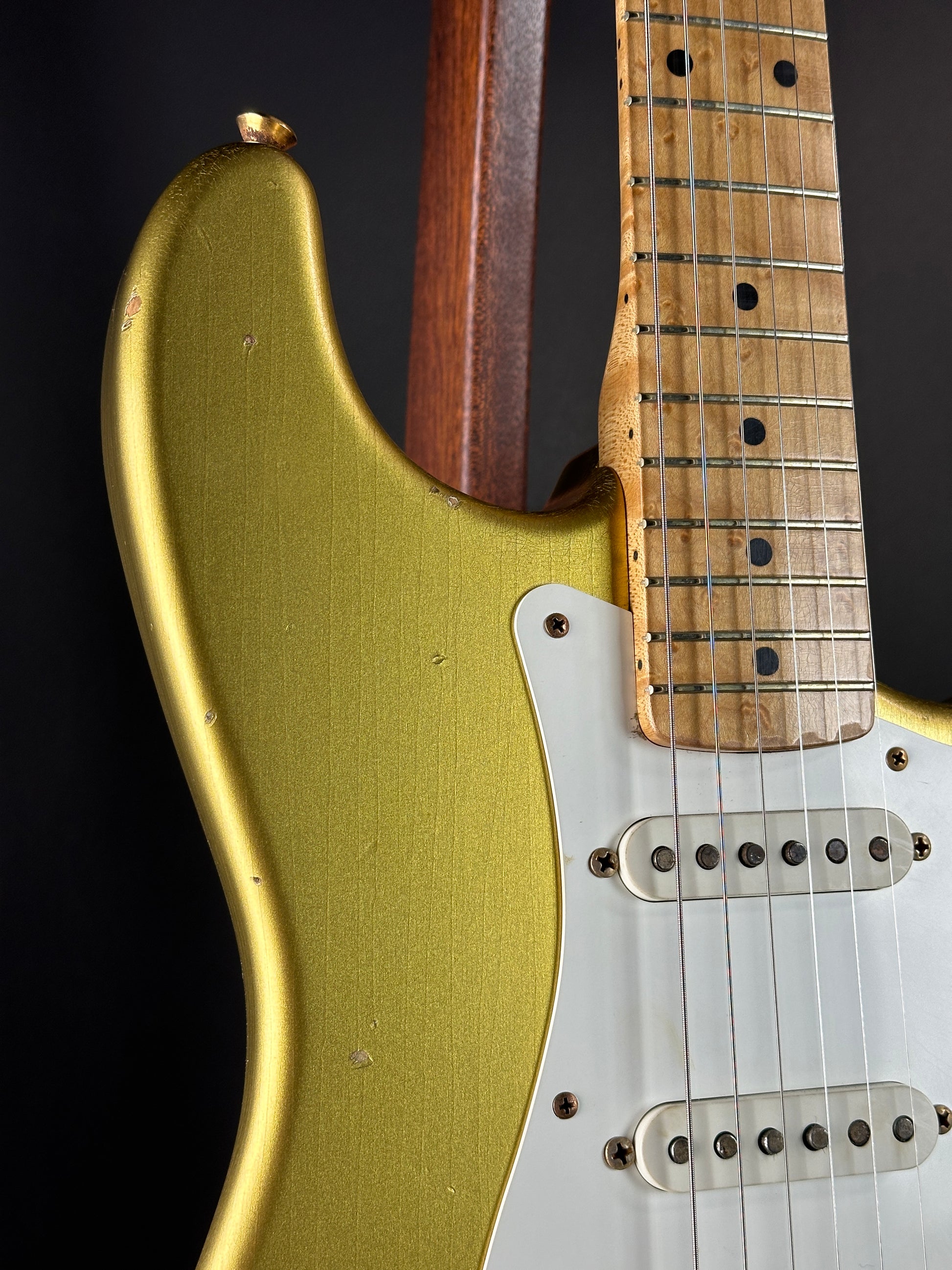 Close-up of a guitar with a gold body and wooden neck on a black background